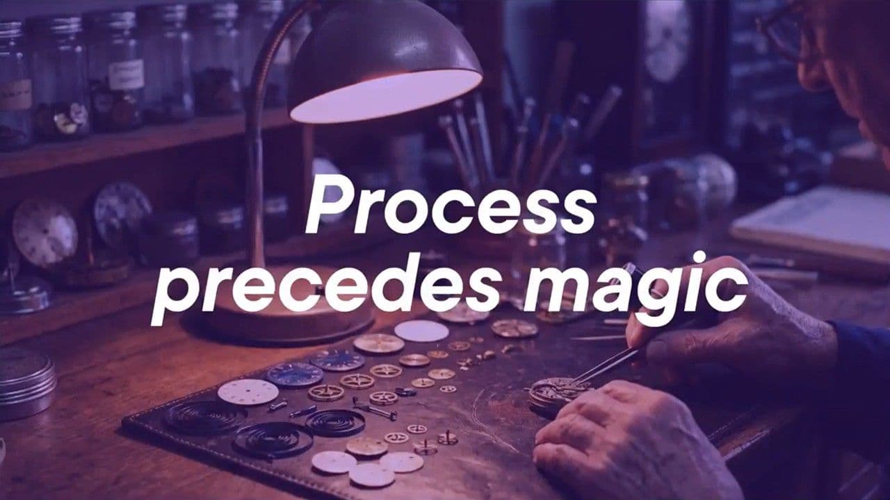 A watchmaker's workbench with intricate parts laid out under a lamp, overlaid with the text Process precedes magic.